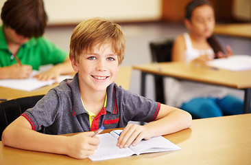 Image showing Portrait, education and learning with a student boy sitting by his desk in a classroom for child development. School, kids and writing with a happy young male child in class to study using a notebook