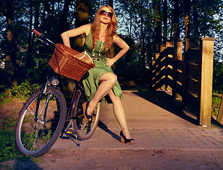 Image showing Style, bridge and bicycle with woman in park for cycling, trend and nature. Happy, smile and fashion with vintage female cyclist and bike resting in countryside for health, summer break or stylish