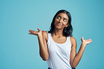 Image showing Comparison, thinking and woman with a choice in a studio with a question, idea or dream. Decision, doubt and Indian female model with option or shrug hand sign by blue background with mockup.