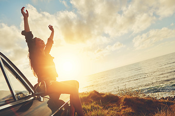 Image showing Road trip, sunset and arms raised with a woman at the coast, sitting on her car bonnet during travel for freedom or escape. Nature, flare and water with a young female tourist traveling in summer