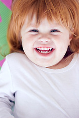 Image showing Young girl, laughing and funny portrait of a baby on a home playpen ground with a smile. Ginger infant, kid laugh and happy in a house with joy, youth and positivity from childhood looking up