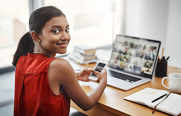 Image showing Business woman, portrait and smile with a phone and laptop at desk for media, research and creative work or blog. Happy Indian female entrepreneur with a smartphone and internet for communication