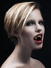 Image showing Portrait, fangs and female vampire in studio on dark background for halloween or cosplay. Fantasy, horror or scary with attractive young woman monster posing as an evil villain with creative makeup