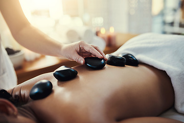 Image showing Woman, hands and rocks for back massage at spa in beauty relaxation or skincare on bed. Hand of masseuse applying hot rock or stones on female for physical therapy, zen or skin treatment at resort