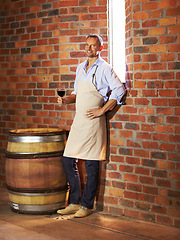 Image showing Portrait, man sommelier with glass and taste in cellar or factory. Alcohol or drink, production storage or industry and happy mature male smile and standing by wooden barrel during wine tasting