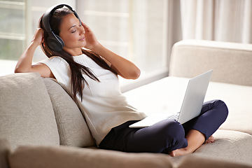 Image showing Headphones, laptop and woman on a home sofa listening to music or audio while streaming online. Calm female person relax on couch to listen to radio or song with internet connection and technology