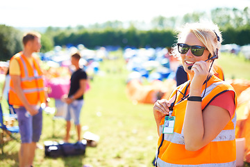 Image showing Festival security, communication and a woman outdoor on a grass field for safety at a music concert. Party, event and crowd control with a female officer using a headset microphone for protection