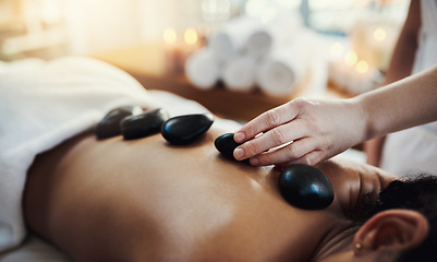 Image showing Woman, hands and rocks in back massage at spa for skincare, beauty or relaxation on bed indoors. Hand of masseuse applying hot rock or stones on female for physical therapy or treatment at resort