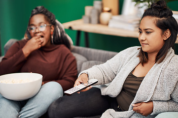 Image showing Girl friends, watching tv and remote in home living room on a couch with snack eating. Series, movie and women together in a lounge with a female friend looking at a television in house with popcorn