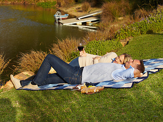 Image showing Couple, picnic and lying by lake with wine outdoor, having fun and bonding on vacation. Portrait, alcohol and man and woman by river to relax, happiness and enjoying romantic time together in summer.