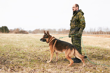 Image showing Male officer, military uniform and german shepherd on leash or dog guarding territory and outdoors. Soldier, pet with rope and in the field for army training or drills or man official in gear outside