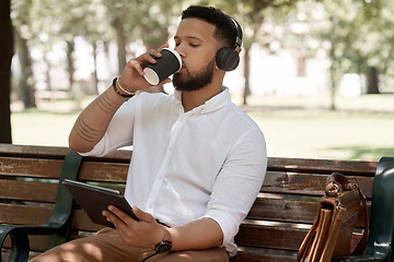 Image showing Business man, coffee and headphones outdoor with a tablet on a park bench for a break with internet. Male entrepreneur person in nature while streaming and listening to music on a audio app to relax