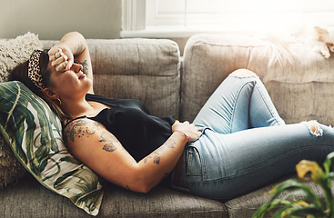 Image showing Period pain, menstrual and a woman on a sofa in the living room of her home suffering from cramps. Stomach, digestion and constipation with a young female person holding her abdomen in discomfort