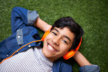 Image showing Boy child, grass and lying with headphones in portrait for music, streaming and online audio with happiness. Male kid, happiness and listening to sound, internet radio or podcast on lawn in garden