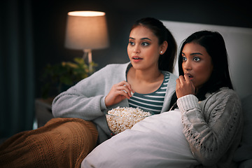 Image showing Popcorn, eating and people or friends with horror movies, scary show and sleepover on bed, streaming service or television. Gen z women relax in bedroom for drama TV film, home cinema or subscription