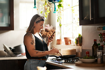 Image showing Happy, woman cooking food with smartphone and in kitchen of a home. Dinner or lunch, multitasking and plus size, natural person with tattoo on cellphone following recipe motivation for healthy diet