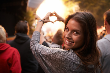 Image showing Portrait, heart and hand gesture with a woman at a concert as part of the crowd or audience of a festival. Face, party and smile with a happy young female person outdoor at a music performance event