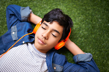 Image showing Headphones, music and boy relax on grass with eyes closed outdoors on holiday, free time and weekend. Calm, peace and face of kid in garden listening to song, track and streaming audio for happiness