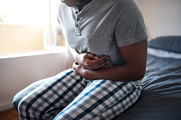 Image showing Man, stomach ache and hands holding belly in a bedroom in a home at morning. African male person, sick and indigestion pain in a house on a bed feeling hurt with abdomen cramp and ibs problem