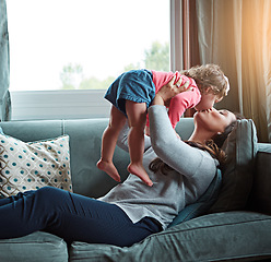 Image showing Mom, kiss and lifting girl on sofa in home living room and relax, bonding and quality time together or mother, love and family happiness. Child, mommy and playing game on couch in house with smile