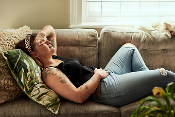 Image showing Period pain, menstruation and a woman on a sofa in the living room of her home suffering from cramps. Stomach, digestion and constipation with a young female person holding her belly in discomfort