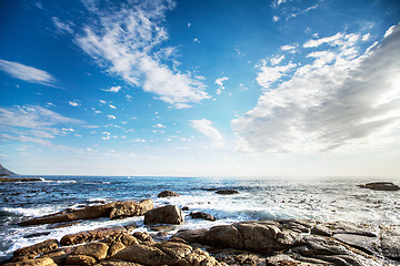 Image showing Rock, ocean and nature with waves at beach for environment, landscape and blue sky. Calm, summer and seascape with sunrise on horizon at coastline for tropical, clouds and water surface