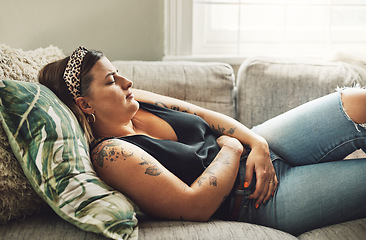 Image showing Period, menstrual pain and a woman on a sofa in the living room of her home with cramps of the abdomen. Stomach, digestion or menstruation with a young female person holding her belly in discomfort