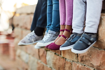 Image showing Shoes, legs of school children and sitting on brick wall together. Group of friends, friendship and young student outside of classroom during lunch period or break time with footwear showing.