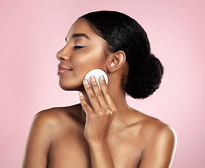 Image showing Skincare, beauty and woman with cotton pad on face, smile and makeup removal with luxury skin product in studio. Dermatology, facial cleansing cosmetics and happy model isolated on pink background.