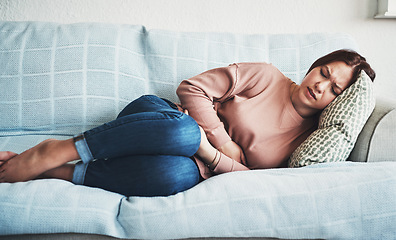 Image showing Woman, stomach ache or pain on home sofa with menstrual or period cramps in lounge. Sick, abdomen or colon problem of a female person with hands on tummy for constipation, digestion or virus