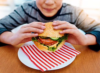 Image showing Child, hands and eating burger on table for delicious lunch, meal or food with healthy vegetables at home. Hand of hungry little boy holding beef hamburger for fresh dinner, nutrition or vitamins