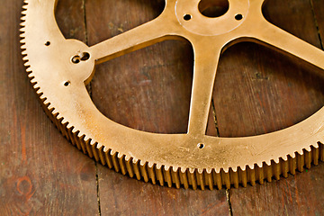 Image showing Clock gear, gold and wheel cog on a wood table with golden machinery and gears. Metal, closeup and steel with machine detail and maintenance on wooden tabletop with brass parts and wheels on surface