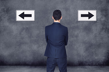 Image showing Back, arrow and direction with a business man planning or brainstorming a decision while in doubt on a wall background. Confused, challenge or strategy with a male employee thinking of a solution