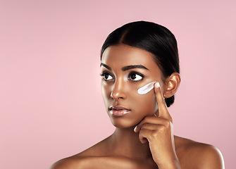 Image showing Thinking, skincare and face of woman with cream in studio isolated on a pink background mockup. Dermatology, creme cosmetics and serious Indian female model apply moisturizer lotion for skin health.