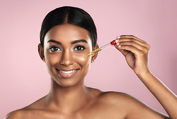 Image showing Face, skincare serum and happy woman in studio isolated on a pink background. Portrait, cosmetics and Indian model with hyaluronic acid, essential oil or vitamin c dropper for healthy dermatology.