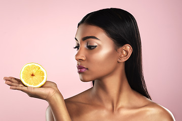 Image showing Face, skincare and woman looking at an orange in studio isolated on a pink background. Fruit, natural cosmetics and Indian female model holding food for healthy diet, nutrition or vitamin c to detox.