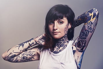 Image showing Portrait, tattoo and edgy with a woman in a tank top on a studio gray background for contemporary style. Fashion, body art and punk with an attractive young female model posing to show her ink