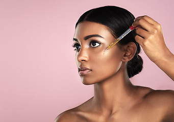 Image showing Face, skincare serum and serious woman in studio isolated on a pink background mockup. Dermatology, cosmetics and Indian model with hyaluronic acid, essential oil or vitamin c dropper for skin health