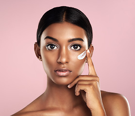 Image showing Portrait, skincare and face of woman with cream in studio isolated on pink background. Dermatology, creme cosmetics and serious Indian female model apply moisturizer lotion for skin health or beauty.