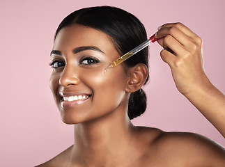 Image showing Face, skincare serum and smile of woman in studio isolated on a pink background. Portrait, cosmetics and Indian model with hyaluronic acid, essential oil or vitamin c dropper for healthy dermatology