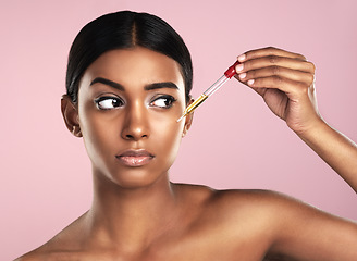 Image showing Face, skincare serum and serious woman in studio isolated on a pink background. Dermatology, cosmetics and Indian model with hyaluronic acid, essential oil or apply vitamin c dropper for healthy skin