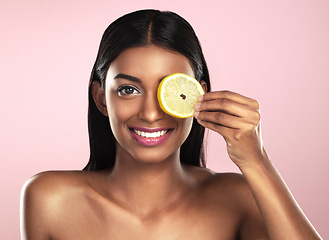 Image showing Face, skincare and smile of woman with a lemon slice in studio isolated on a pink background. Fruit, natural cosmetics and portrait of Indian female model with food for detox, nutrition and vitamin c