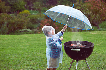 Image showing Weather, nature and boy with a grill, rain and wellness with safety, cover and winter outfit. Bbq, male child or kid with umbrella, cold or young person with food, raincoat or outdoor with protection