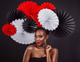 Image showing Portrait, skincare and black woman with origami fans in studio isolated on a dark background. Face, makeup cosmetics and beauty of African female model with traditional Japanese paper hat for fashion