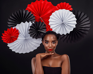 Image showing Face, aesthetic and black woman with origami fans in studio isolated on a dark background. Beauty portrait, makeup cosmetics and skincare of female model with traditional Japanese art for fashion hat