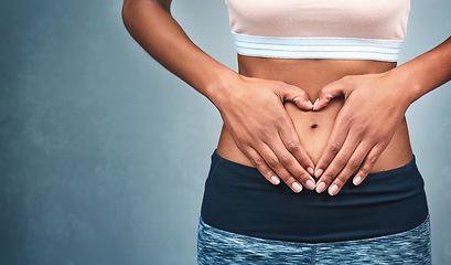 Image showing Heart, fitness and hands of a woman on a stomach isolated on a dark background in studio. Wellness, gut health and a girl with shape for love of body, weight loss and abdomen digestion on backdrop