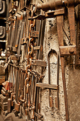 Image showing Steel, tools and workshop with blacksmith workplace and industrial factory wall background. Artisan, retro and metal tool for manufacturing, warehouse and brass forge industry equipment hanging