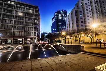 Image showing Night, cityscape and urban buildings at dark with lights in Cape Town outdoor with no people. Street, lighting and city infrastructure with fountain and skyline at evening outdoors with a road