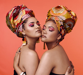 Image showing Fashion, beauty and African women hug on orange background with cosmetics, makeup and accessories. Glamour, luxury and female people with exotic jewelry, traditional style and head scarf in studio