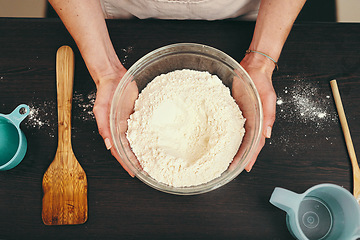 Image showing Woman, hands and bowl of flour for baking above with ingredients or recipe on kitchen counter at home. Top view of female person or baker hand holding mixture or batter for delicious pastry in house